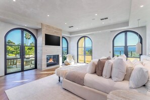 Un dormitorio amplio con chimenea, ventanas arqueadas grandes y vista al mar.