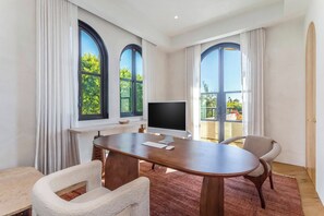 A modern meeting room with a large table, two chairs, a computer monitor, and large windows with a view of greenery.