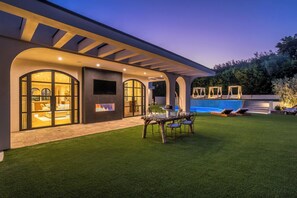 A modern house with a swimming pool, outdoor seating, and a well-lit patio area.