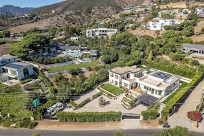 A large, modern house with a swimming pool, surrounded by lush greenery and hills.