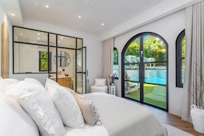 Un dormitorio moderno con una cama grande, un baño con espejo y vista a una piscina.
