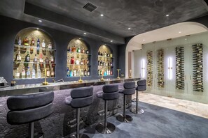 Un espace bar doté de plusieurs étagères remplies de bouteilles d’alcool, d’un comptoir en marbre et de tabourets de bar.