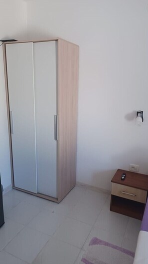 Ein Zimmer mit einem Schrank, einem kleinen Holztisch mit Schublade und einem Lichtschalter an der Wand.