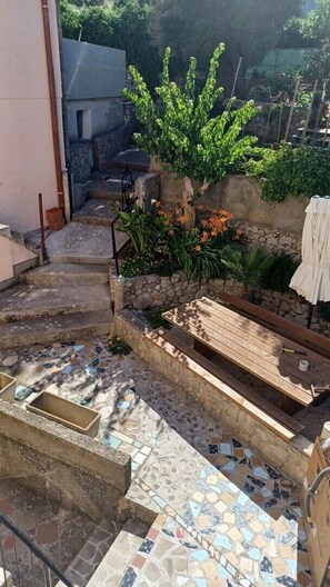 Eine Terrasse mit Mosaikboden, einer Holzbank und einer Pflanze mit orangefarbenen Blüten.