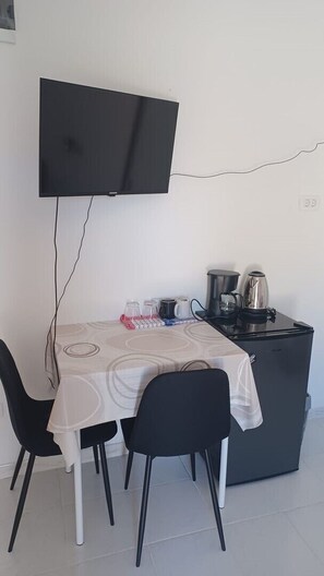 Eine kleine Küchenzeile mit Kaffeemaschine, Wasserkocher und Mikrowelle. Es gibt einen Tisch mit Stühlen und einen an der Wand montierten Fernseher.