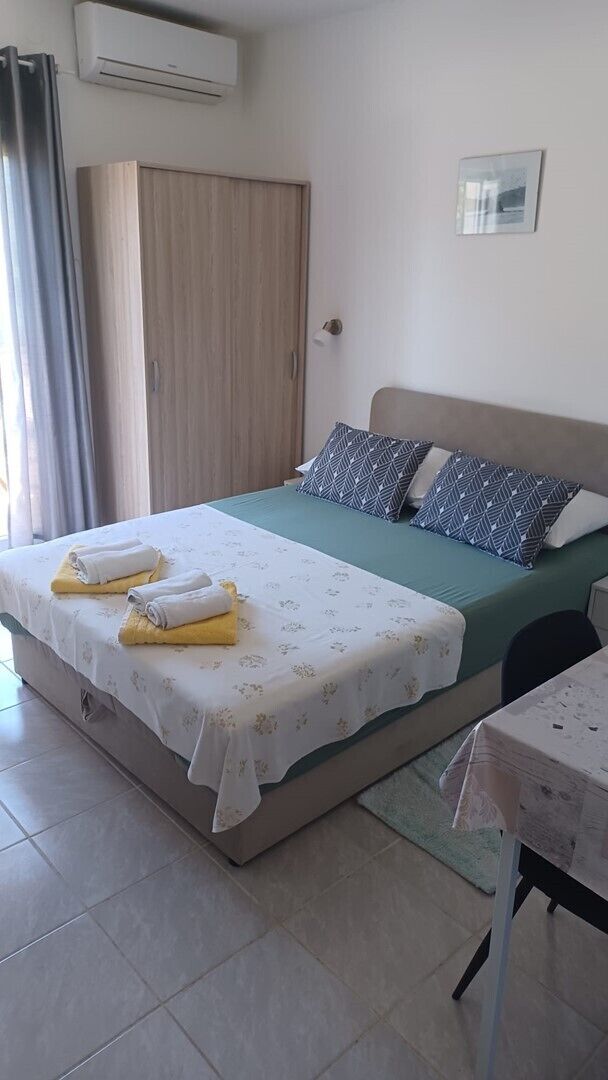 Une chambre à coucher comprenant un lit, des oreillers, une table, une armoire et un appareil de climatisation.