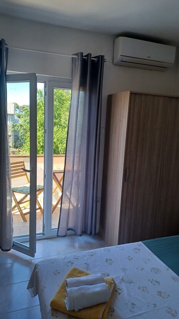 Een slaapkamer met een bed, een kledingkast, een schuifdeur naar een buitenruimte en een airconditioningsunit.