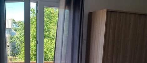 A bedroom with a bed, a wardrobe, a sliding glass door to an outdoor area, and an air conditioning unit.