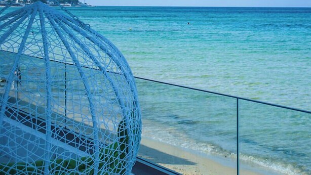 Vista de playa con una estructura de malla, una barandilla y cielo despejado.