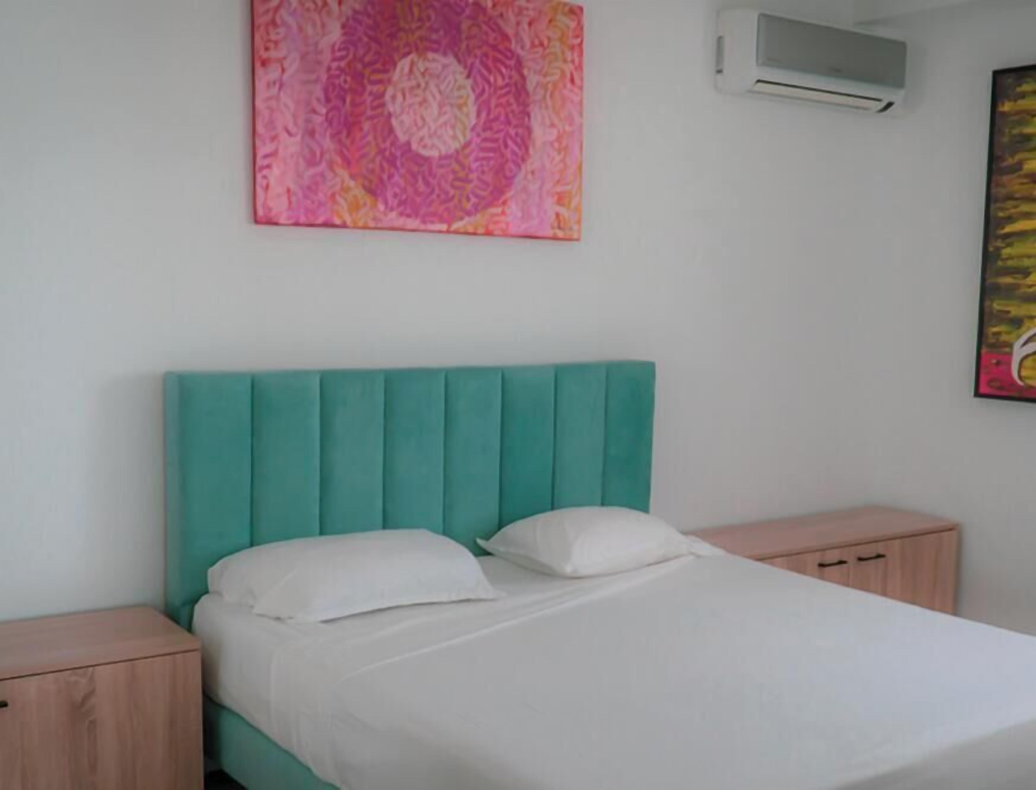 Un lit avec une tête de lit de couleur turquoise, une literie blanche et deux tables de chevet.