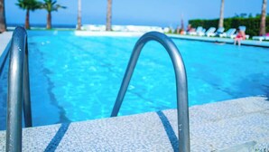 Una piscina con agua cristalina, rodeada de sillones de descanso y palmeras.