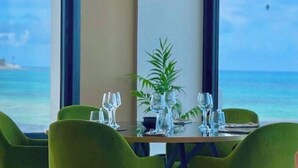 Mesa de comedor con cristalería y una planta, con vista a la playa.