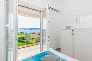 Ein Balkon mit Blick auf das Meer und Gebäude, ein weißes Schränkchen und ein blaues Handtuch auf dem Boden.