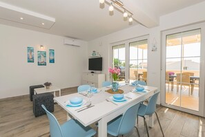 A dining area with a white table, blue chairs, and a TV on the wall. - Villa Sunset sea row (Medulin)