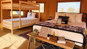 Una habitación acogedora con dos literas, un ventanal grande, una mesita de noche con una planta y un cartel con nombres de redes sociales.