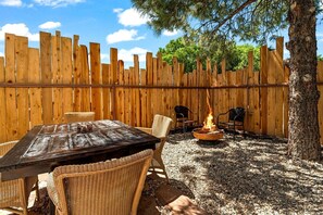 Una cerca de madera, un hogar para fuego, sillas de mimbre y una mesa en un entorno al aire libre.