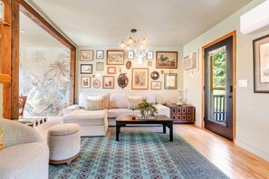 Ein Wohnzimmer mit Sofa, Hocker, Couchtisch und einem gemusterten Teppich.
