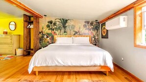 A bedroom with a bed, wooden floor, a mural on the wall, a dresser, and an air conditioning unit. - The Catskill | Three Retreats One Creekside Escape (Jefferson Heights)