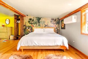 Ein Schlafzimmer mit Bett, Holzboden, Wandgemälde, Kommode und Klimaanlage.