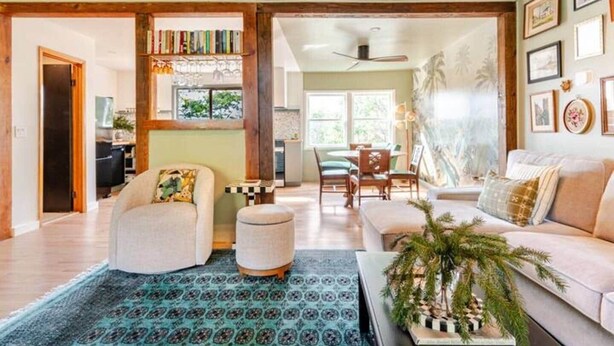A spacious living room with a sofa, ottoman, and a dining area with chairs and a table. - The Catskill | Three Retreats One Creekside Escape (Jefferson Heights)