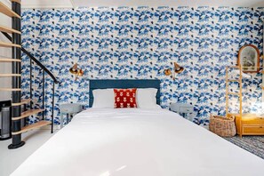A bedroom with a bed, two bedside lamps, a headboard, a wooden ladder, a small table, and a wall with a blue and white floral pattern. - The Catskill | Three Retreats One Creekside Escape (Jefferson Heights)