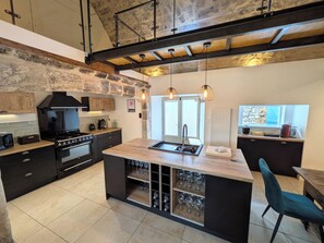 A modern kitchen with a central island, built-in wine storage, and a stone accent wall. - La Louverie | Private Jacuzzi | View of the Gorges du Tarn (Mostuéjouls)