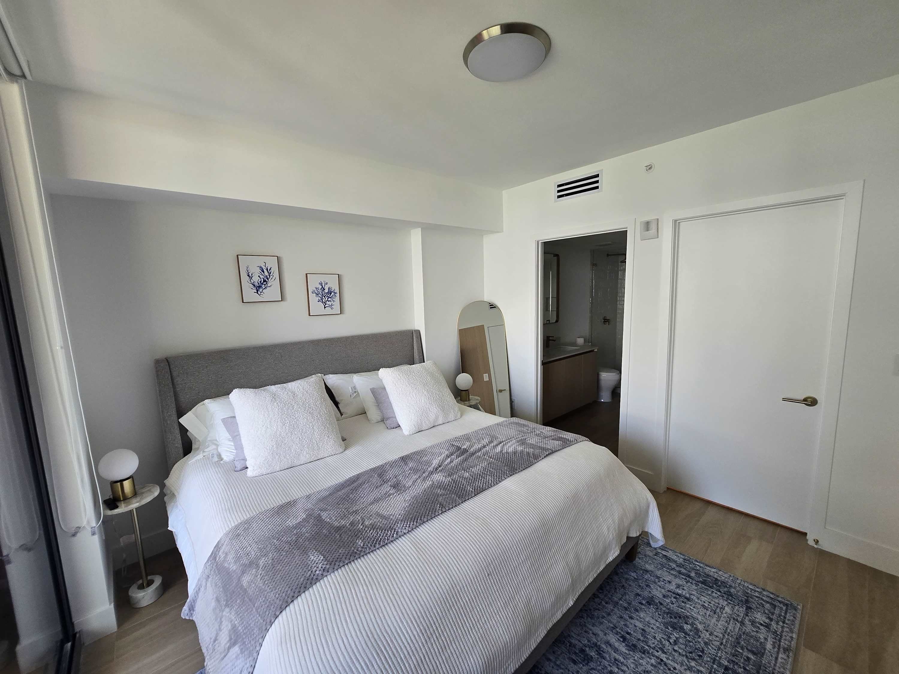 Een moderne slaapkamer met een bed, nachtkastjes, een spiegel en een deur naar de badkamer.