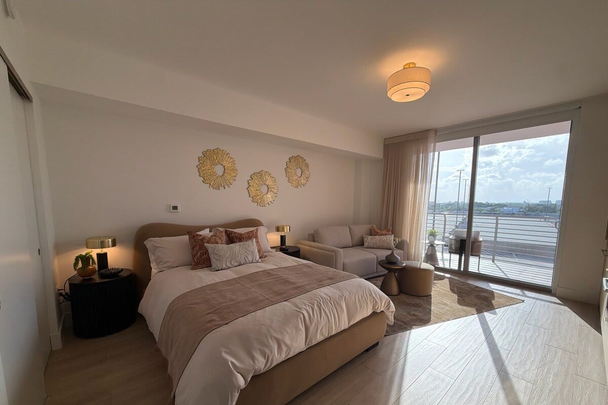 A spacious bedroom with a large bed, a sofa, and a view of the city through large windows.