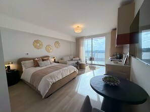 Een moderne hotelkamer met een groot bed, een zithoek, een eettafel en uitzicht op zee.
