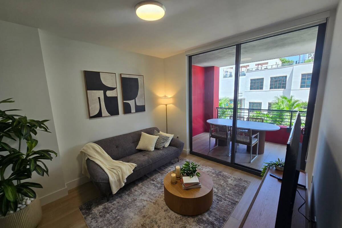 A modern living room with a grey sofa, a round coffee table, and a large sliding glass door leading to an outdoor balcony.