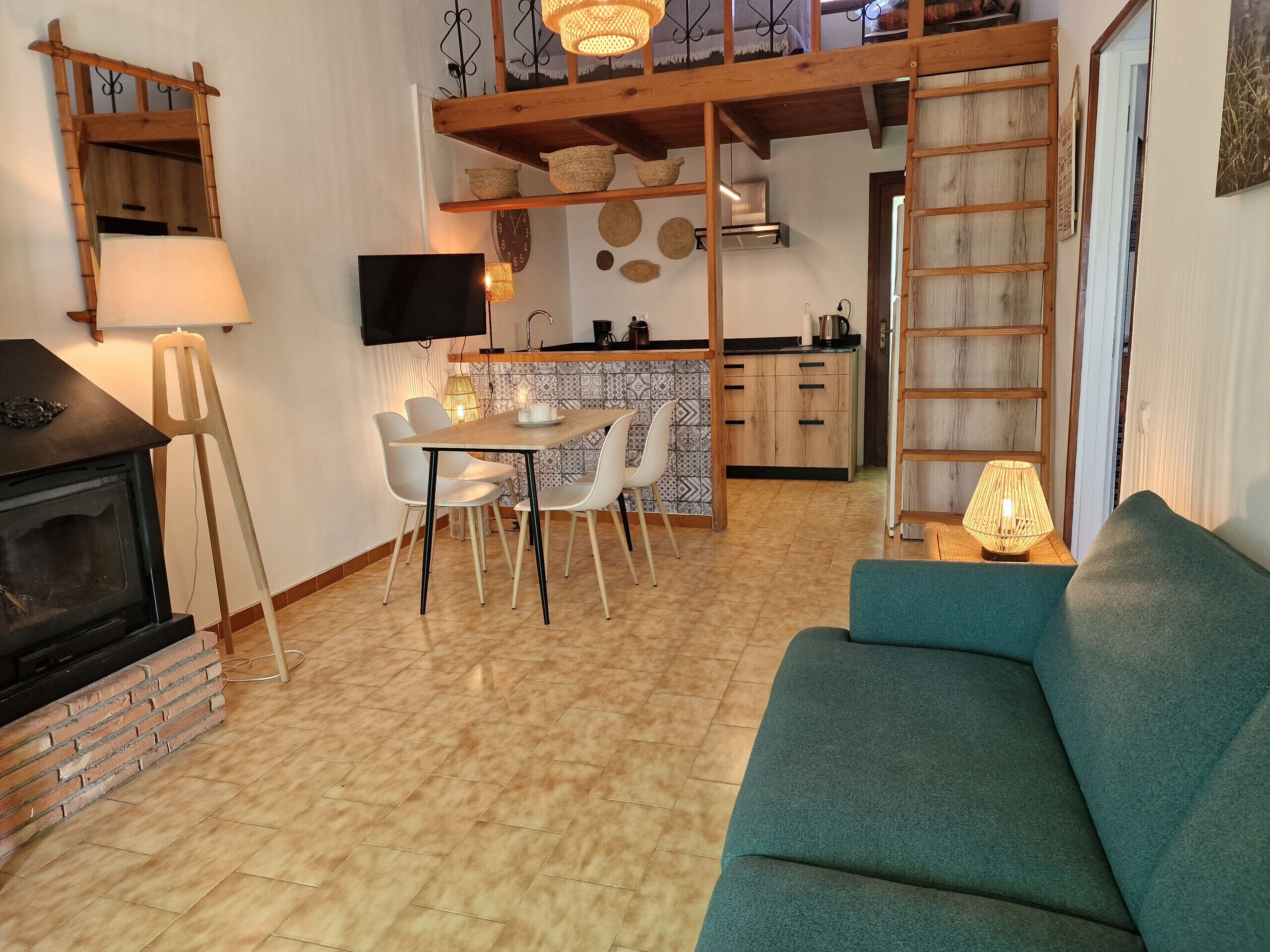 A cozy living room with a fireplace, a dining area with chairs, a kitchen with a wooden counter, and a loft space with a ladder.