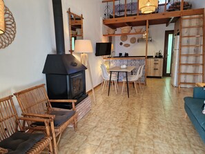 A cozy living room with a fireplace, wicker chairs, a dining table, and a kitchen area. - "Maritim"@MARISOL: 50m to the beach, private pool, A/C, WiFi, dog beach (Riumar)