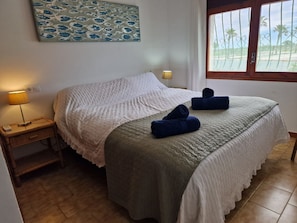 A neatly made bed with a white and green bedspread, a bedside lamp, and a window with a view of palm trees. - "Maritim"@MARISOL: 50m to the beach, private pool, A/C, WiFi, dog beach (Riumar)