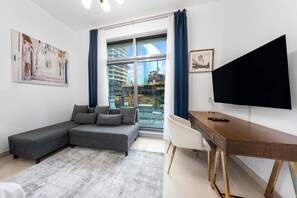 Ein modernes Wohnzimmer mit einem grauen Ecksofa, einem Holztisch, einem Flachbildfernseher und einem Balkon mit Blick auf die Stadt.
