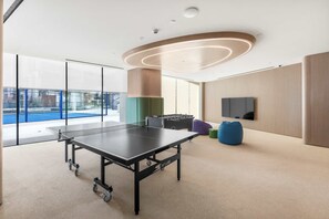 Ein Tischtennistisch in einem modernen Raum mit großen Fenstern, einem Flachbildfernseher und einer Couch.