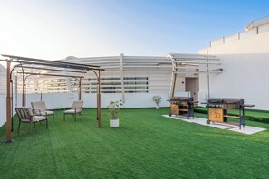 Eine Dachterrasse mit Kunstgrasanlage, Gartenmöbeln, einem Grill und einer Pergola.