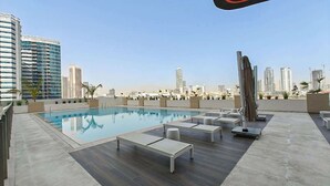 Una piscina sul tetto con sedie a sdraio, una scultura moderna e lo skyline della città sullo sfondo.