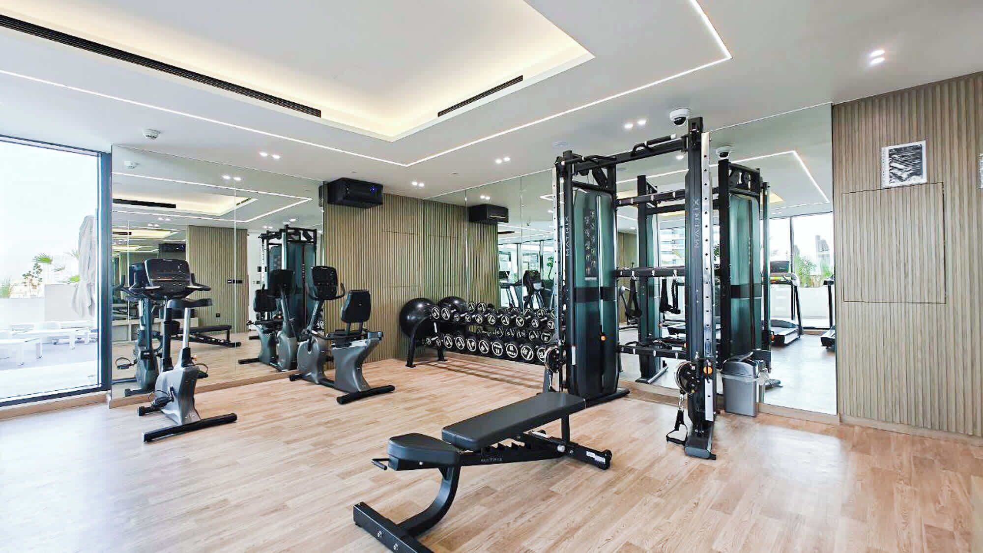 A modern gym with various exercise equipment, large windows, and a clean, spacious layout.