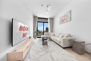Ein modernes Wohnzimmer mit einem großen Flachbildfernseher, einer Couch, einem Couchtisch und Blick auf die Stadt durch große Fenster.