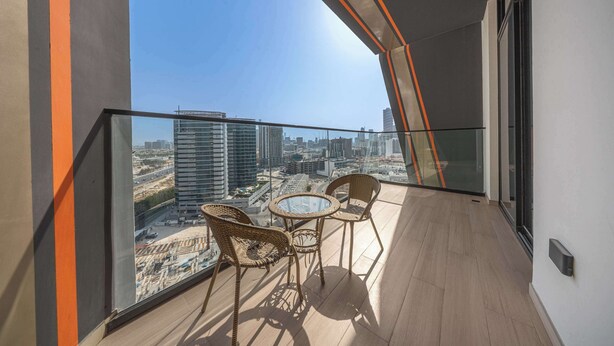 Un balcone con ringhiera in vetro, sedie in vimini, un tavolino rotondo e vista sulla città.