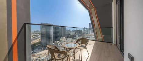 Un balcon doté d'une balustrade en verre, de chaises en osier, d'une petite table ronde et offrant une vue sur la ville.