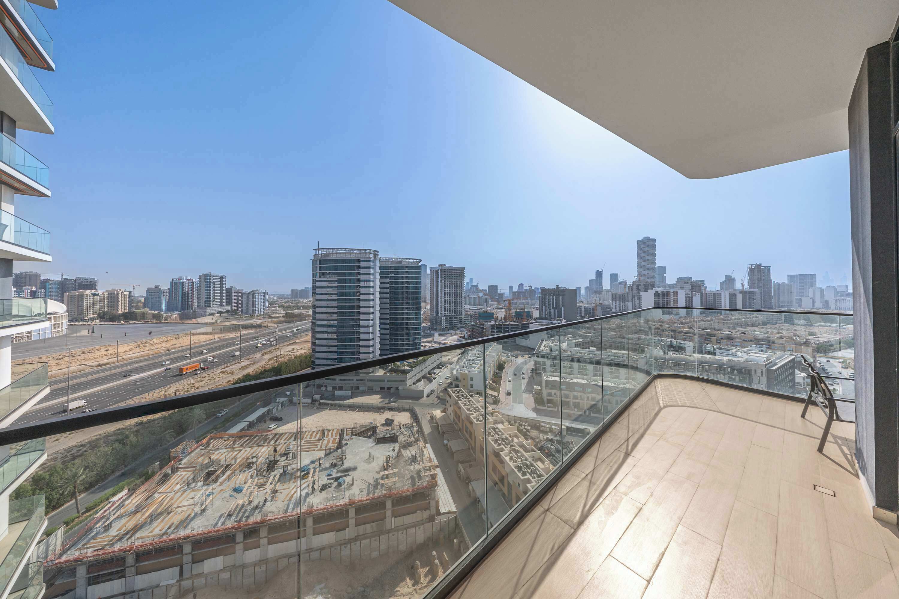 A balcony with a city view, glass railings, and a clear sky.