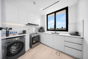 Eine moderne Küche mit Waschmaschine, Backofen und einem großen Fenster mit Blick auf die Stadt.