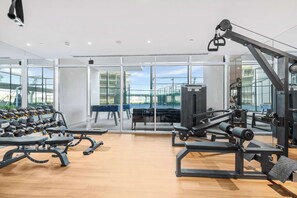 Ein modernes Fitnessstudio mit unterschiedlichen Trainingsgeräten, großen Fenstern und Blick ins Freie.