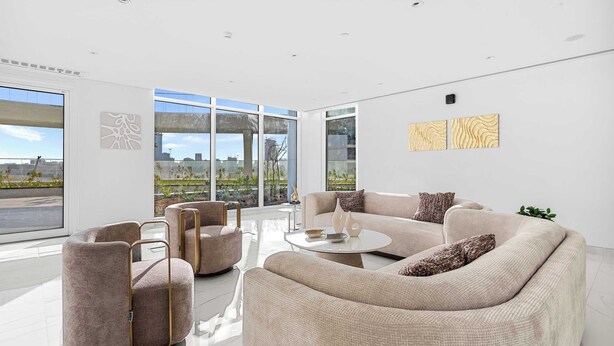Ein modernes Wohnzimmer mit einer großen Couch, Sesseln und einem Couchtisch. Große Fenster bieten Blick auf die Stadt.