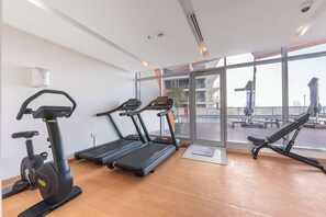 Ein Fitnessstudio mit Laufbändern, Crosstrainern und Rudergeräten, großen Fenstern und Blick auf die Stadt.