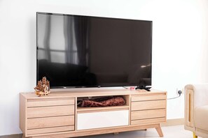 Ein Flachbildfernseher an einem hölzernen TV-Schrank mit Schubladen und Ablagefläche, ein kleines Schiffmodell und eine Fernbedienung.
