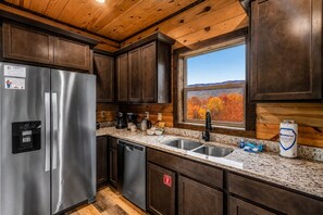 A modern kitchen with a stainless steel refrigerator, a coffee maker, and a sink with a window above it. - Panoramic Views Cabin/ HotTub/ Arcade/ Ski/ Pickleball/ Golf in Gatlinburg,TN (Gatlinburg)