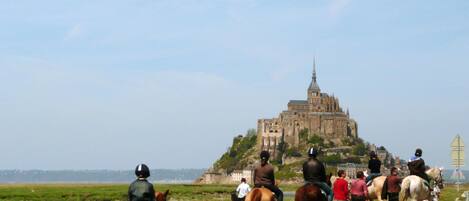 Un groupe de personnes à cheval, suivant un sentier, avec un bâtiment historique en arrière-plan.