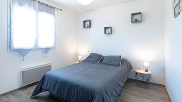Un dormitorio con cama, dos mesitas de noche con lámparas, un radiador y una ventana con cortinas.